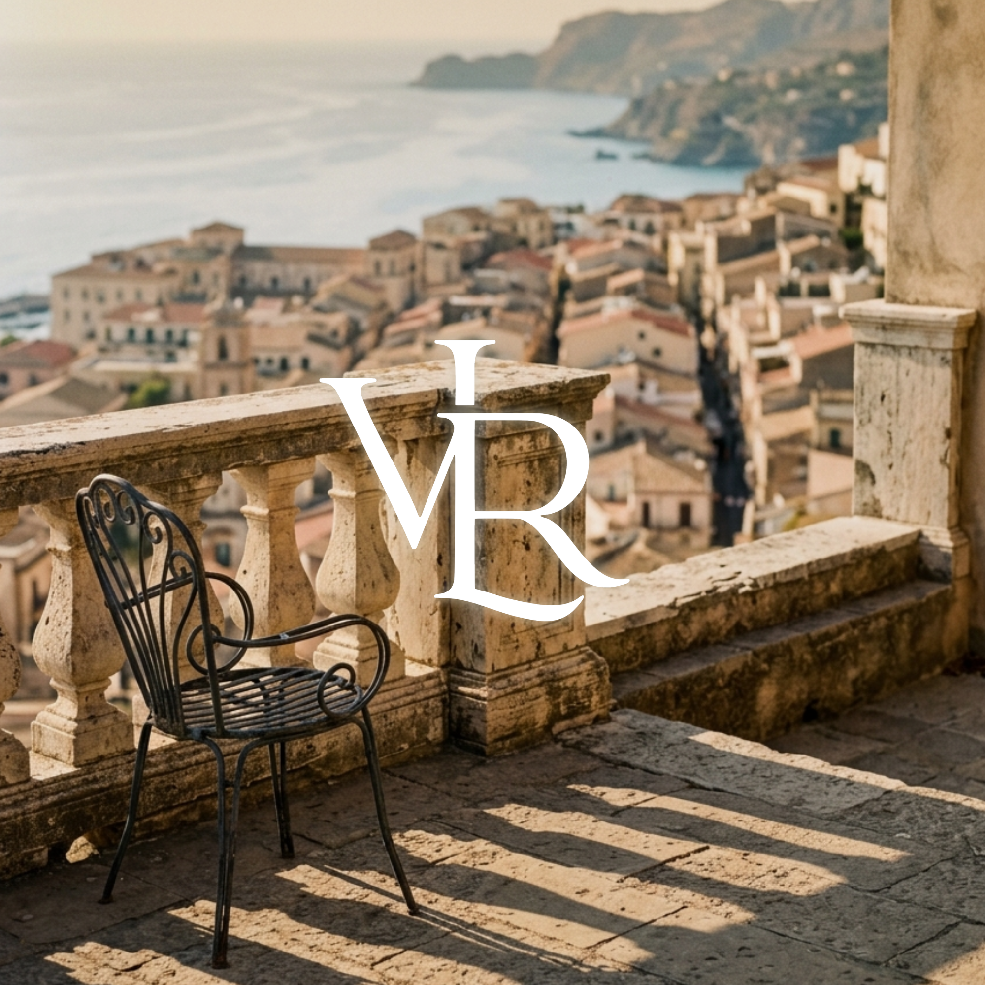 A wrought-iron chair on a terrace overlooking a Sicilian coastal town at golden hour